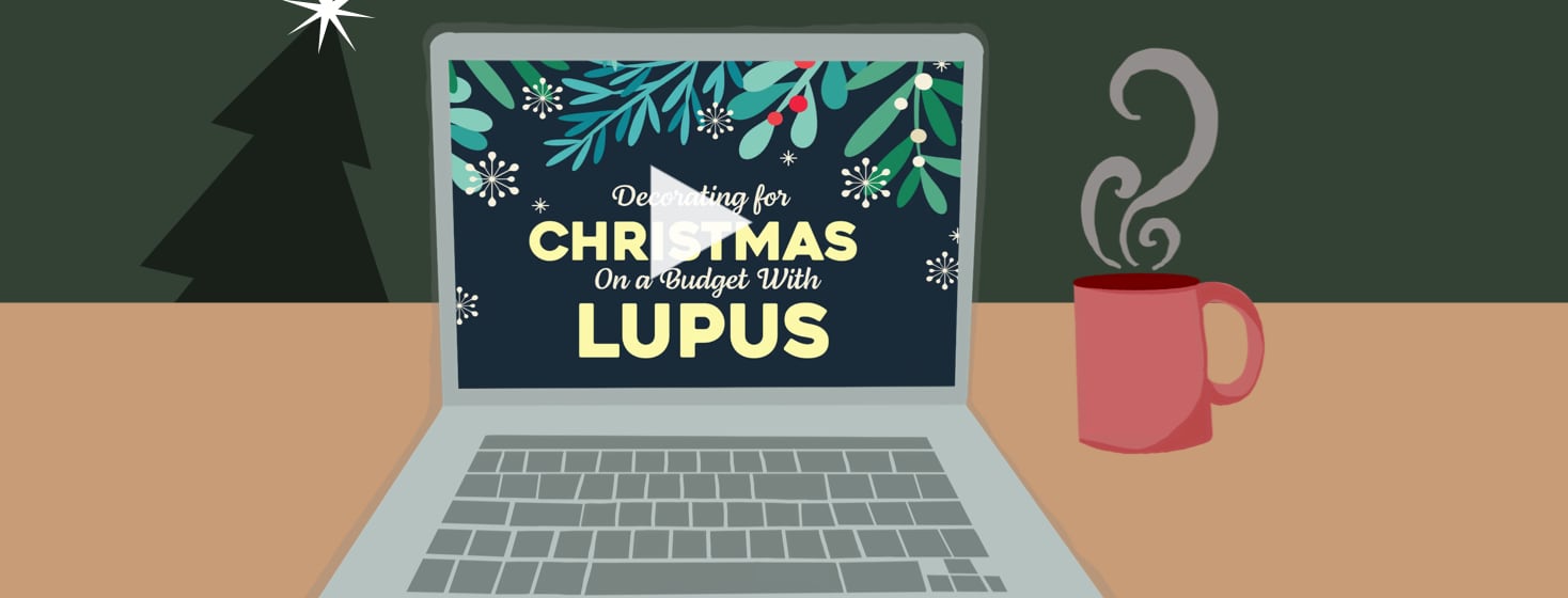 A laptop sitting next to a red steamy mug of coffee. Theres a christmas tree in the background. The laptop screen reads, "Decorating for Christmas on a Budget with Lupus"