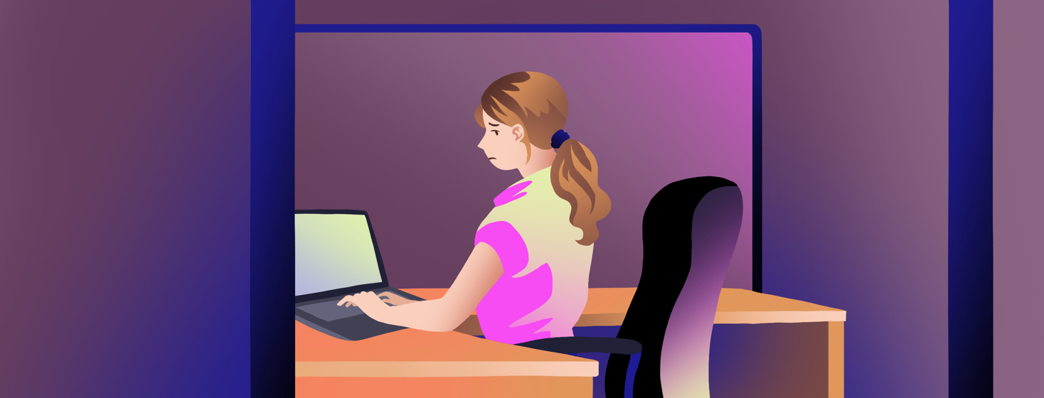 A woman types at a laptop in a work cubicle as she looks over her shoulder with a worried expression.